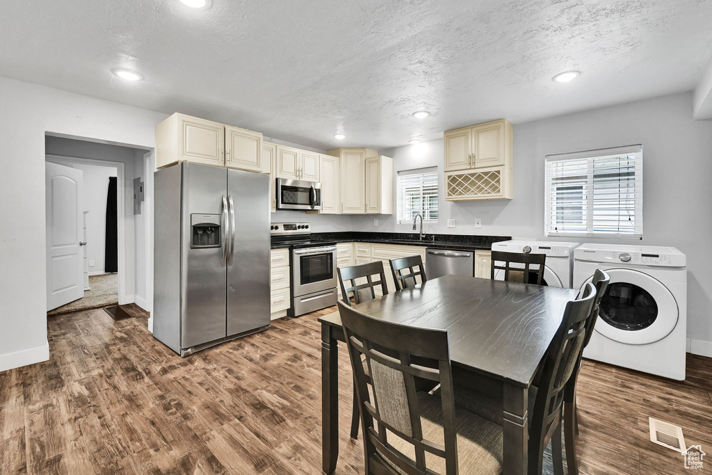 Kitchen with appliances with stainless steel finishes, washer / dryer, cream cabinetry, dark wood-type flooring, and a textured ceiling