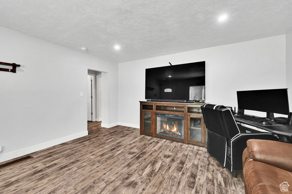 Living room with wood finished floors, baseboards, a textured ceiling, and a glass covered fireplace