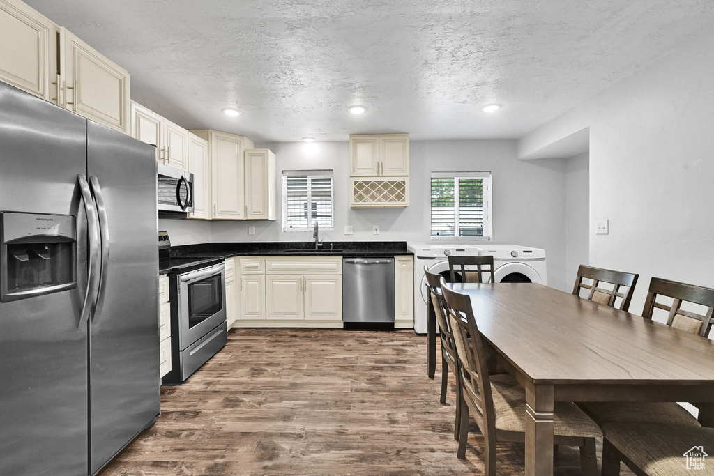 Kitchen with appliances with stainless steel finishes, a sink, dark wood finished floors, a textured ceiling, and dark countertops
