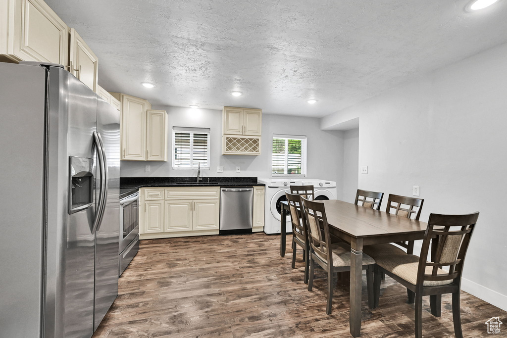 Kitchen with appliances with stainless steel finishes, washer / clothes dryer, a sink, dark wood finished floors, and a textured ceiling