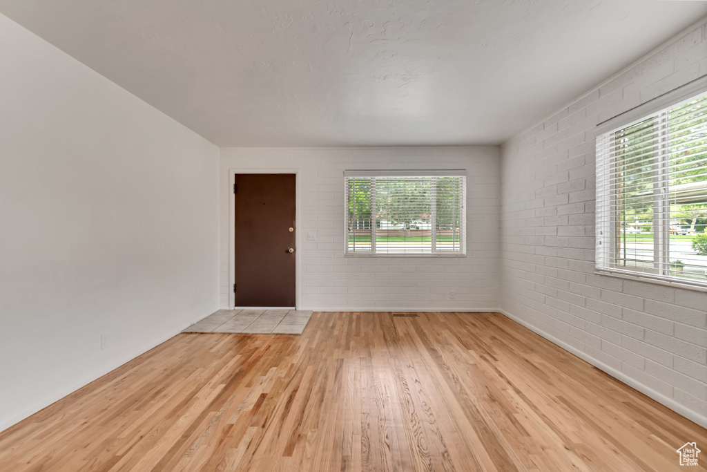 Empty room featuring wood finished floors, plenty of natural light, brick wall, and baseboards