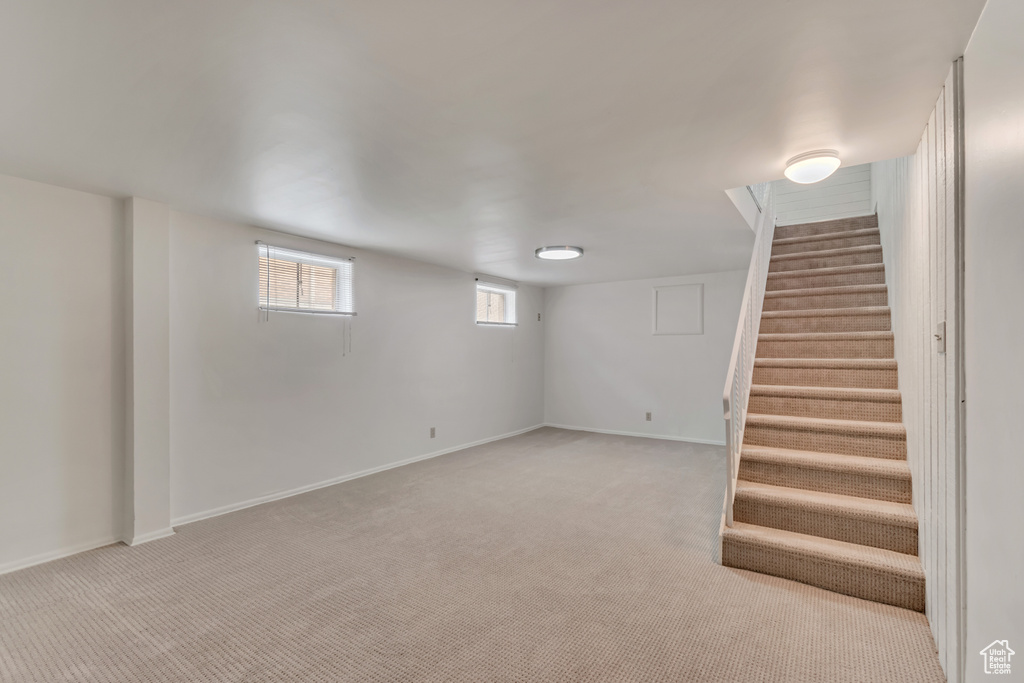 Below grade area featuring light colored carpet, stairway, and baseboards