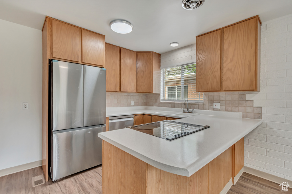 Kitchen featuring stainless steel appliances, a sink, a peninsula, baseboards, and light countertops