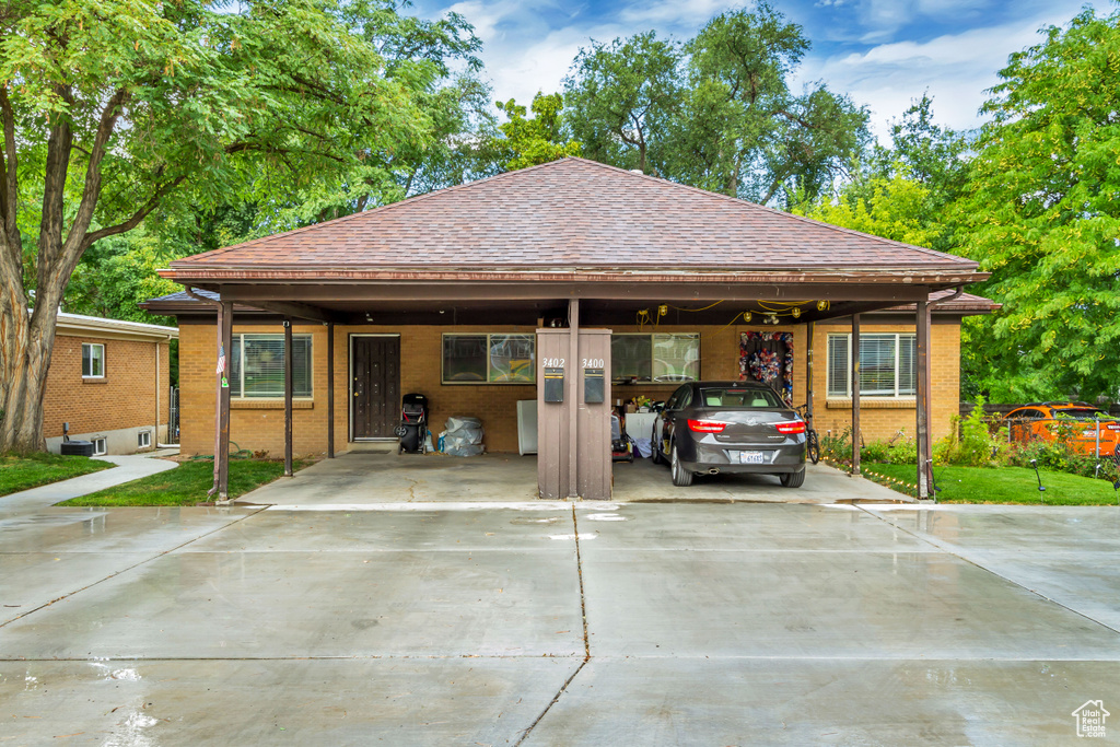 View of front of house featuring concrete driveway, brick siding, roof with shingles, and a carport