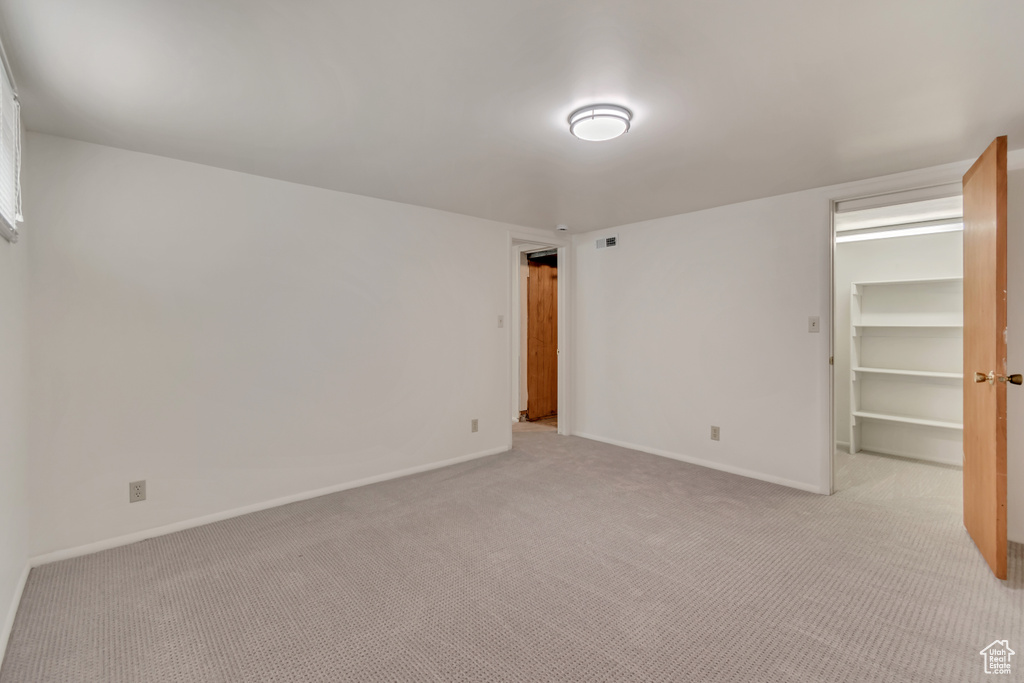 Unfurnished bedroom featuring light colored carpet, a walk in closet, and baseboards