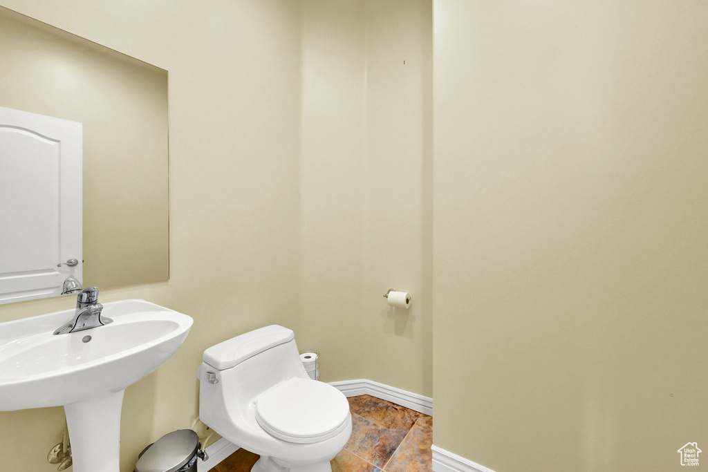 Bathroom featuring a sink, toilet, baseboards, and stone tile flooring