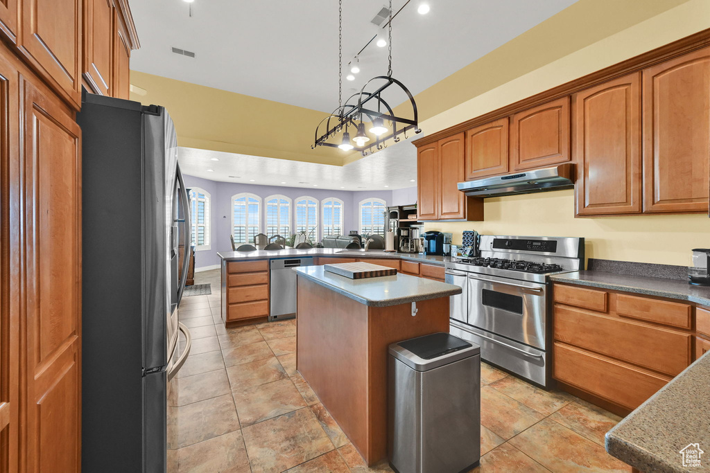 Kitchen featuring a peninsula, a sink, under cabinet range hood, appliances with stainless steel finishes, and a kitchen island