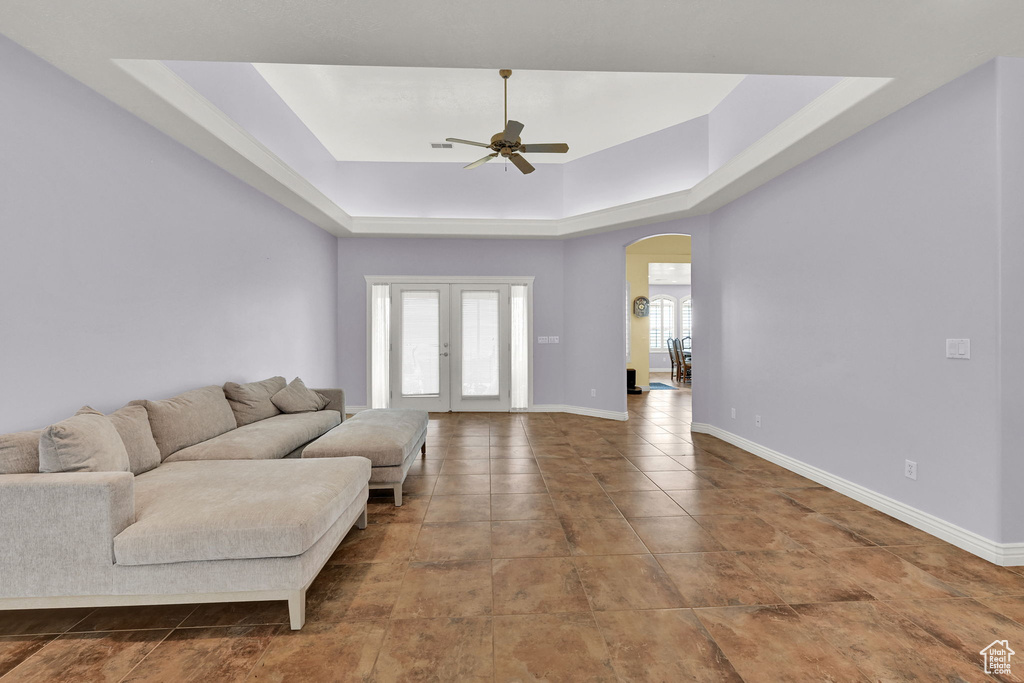 Living area featuring french doors, arched walkways, a ceiling fan, a tray ceiling, and baseboards