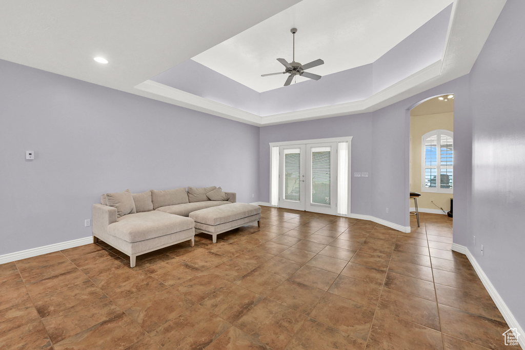 Living room featuring tile patterned floors, arched walkways, a ceiling fan, a tray ceiling, and baseboards