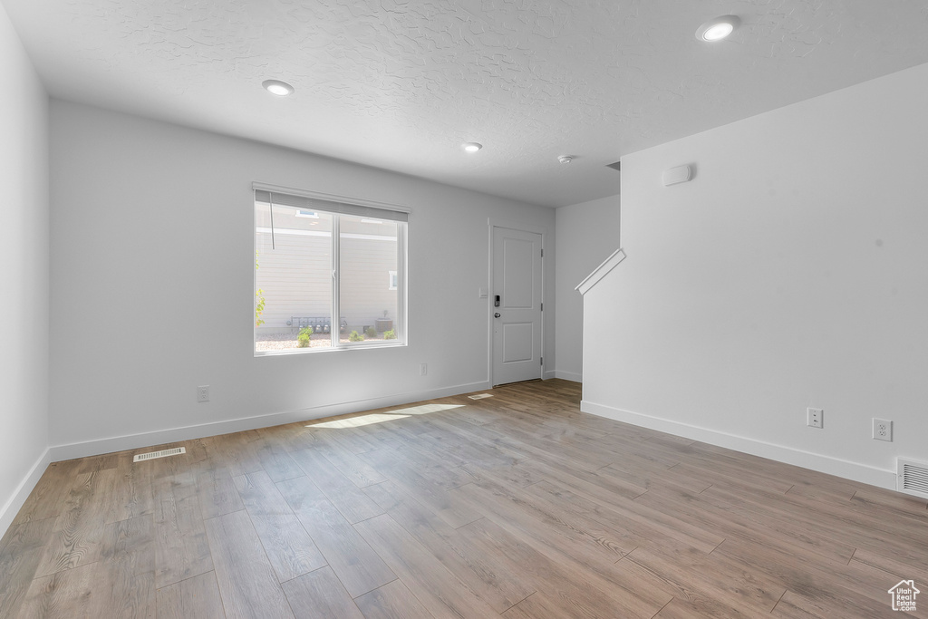 Unfurnished living room with light wood-style floors, baseboards, a textured ceiling, and recessed lighting