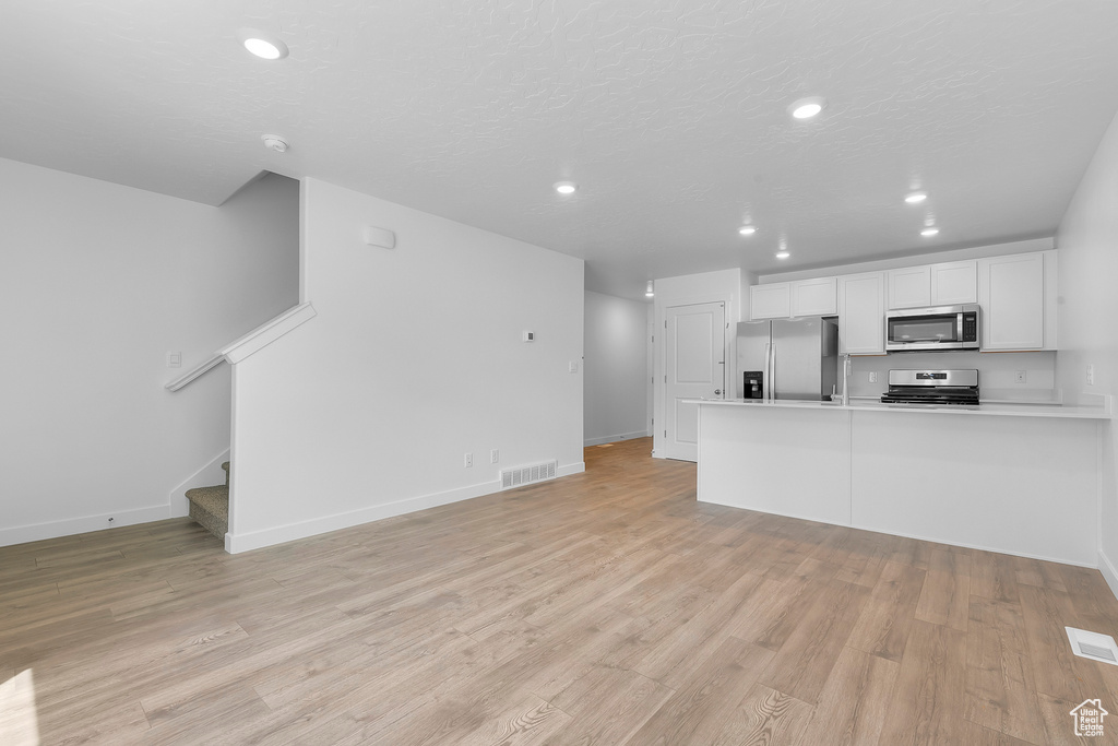 Unfurnished living room with recessed lighting, light wood finished floors, stairway, and baseboards