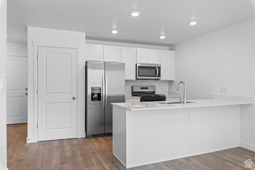 Kitchen with stainless steel appliances, a sink, a peninsula, white cabinetry, and wood finished floors