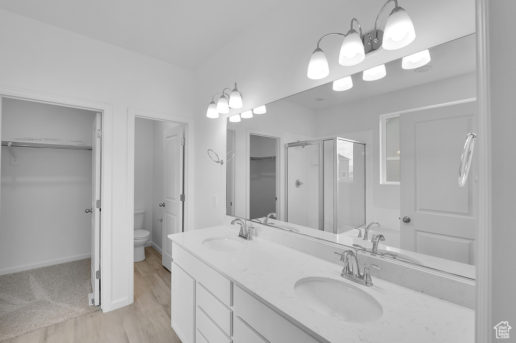 Full bathroom with toilet, a shower stall, double vanity, wood finished floors, and a spacious closet