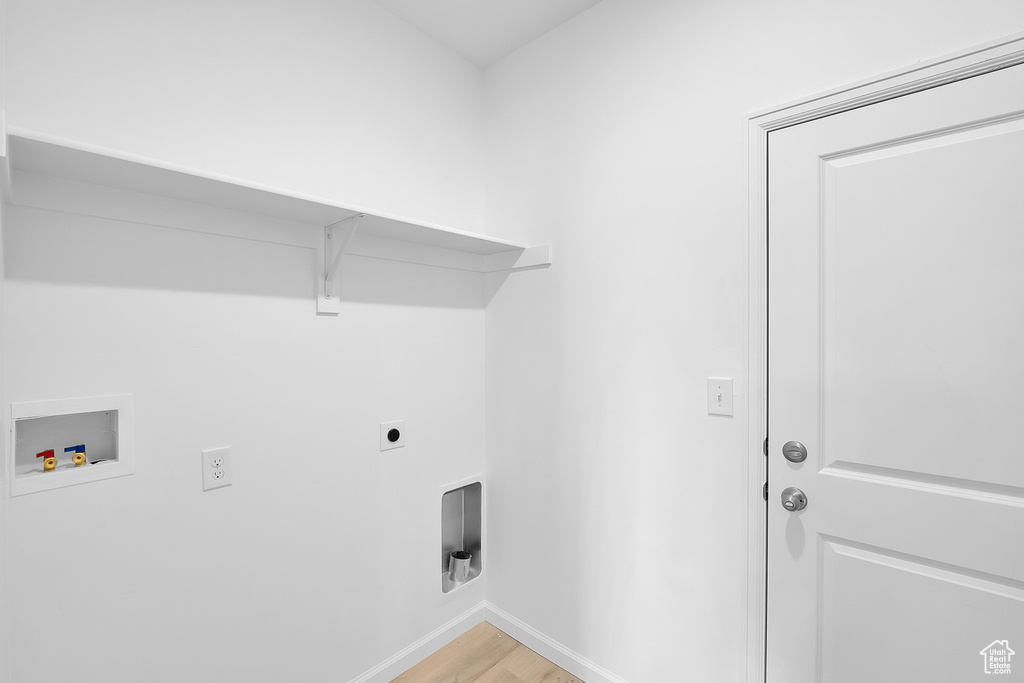 Clothes washing area with electric dryer hookup, hookup for a washing machine, light wood-type flooring, and baseboards