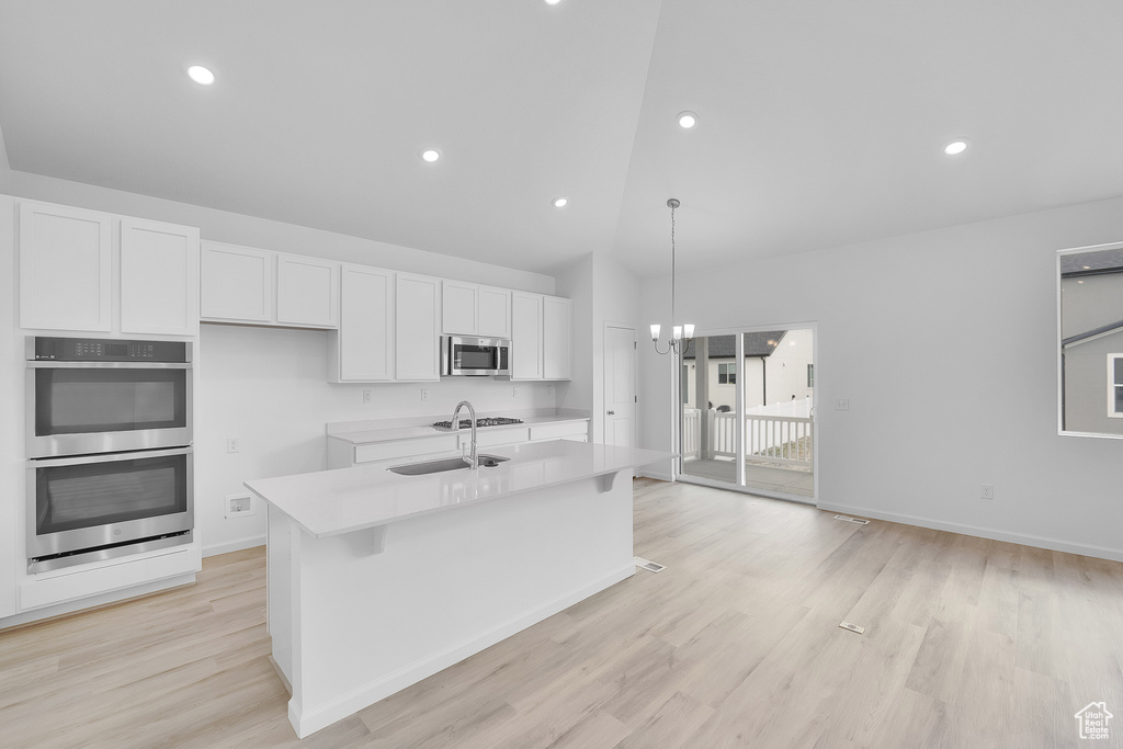 Kitchen featuring appliances with stainless steel finishes, white cabinetry, light countertops, a kitchen island with sink, and light wood-style floors