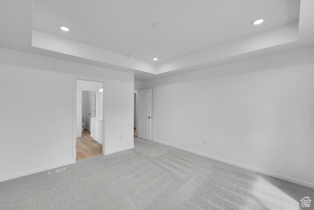 Unfurnished bedroom featuring a tray ceiling, light colored carpet, recessed lighting, baseboards, and connected bathroom