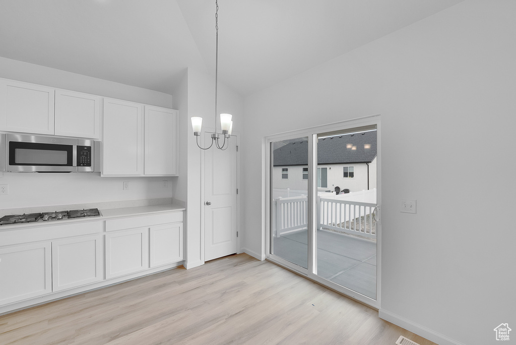 Kitchen featuring stainless steel microwave, light wood-type flooring, a chandelier, white cabinets, and baseboards