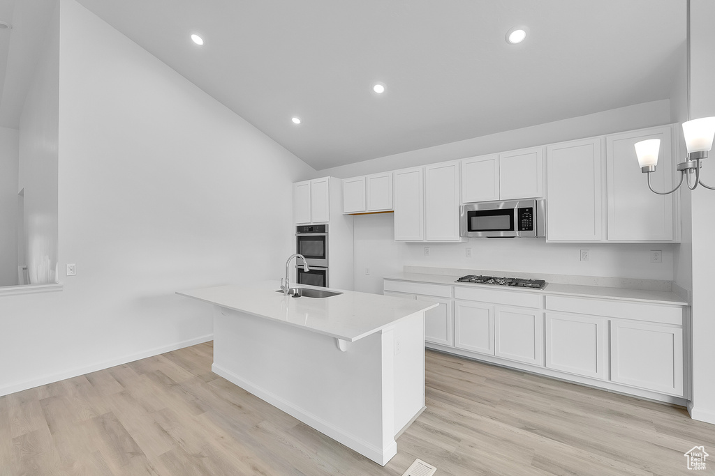 Kitchen with stainless steel appliances, lofted ceiling, a sink, white cabinets, and light countertops