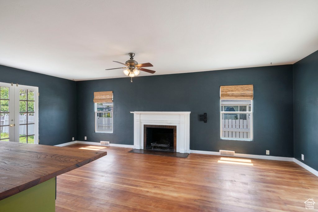 Unfurnished living room with a ceiling fan, a fireplace with flush hearth, wood finished floors, baseboards, and french doors