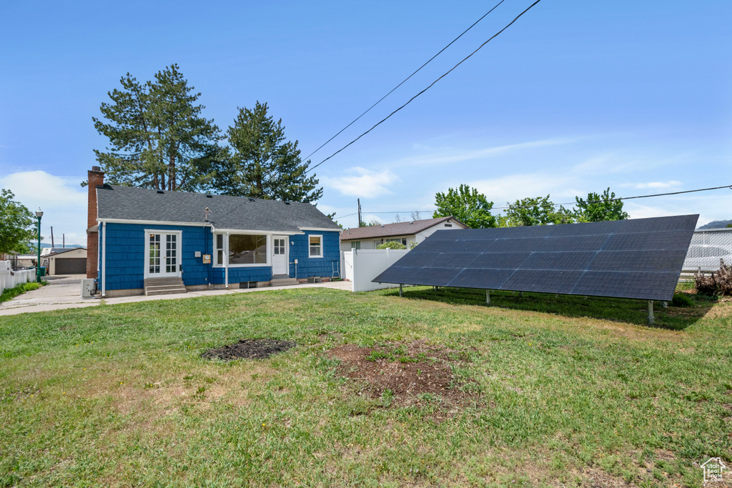 Back of house with entry steps, solar panels, a chimney, and roof with shingles
