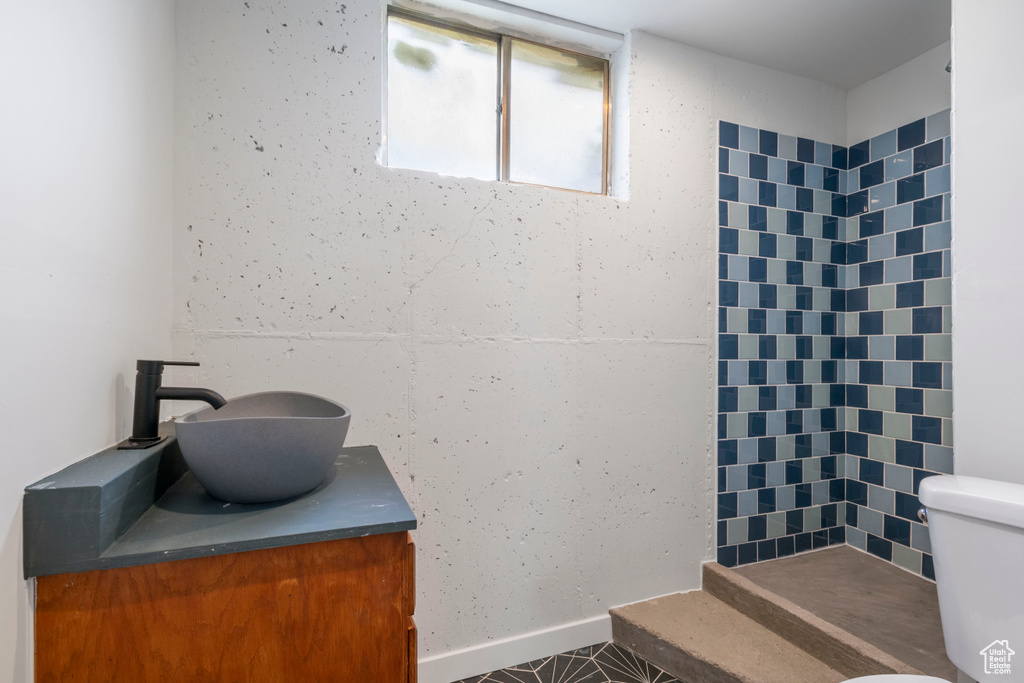Bathroom featuring toilet, a tile shower, and vanity