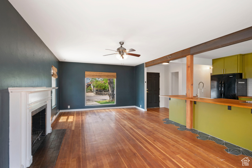 Unfurnished living room with a ceiling fan, hardwood / wood-style flooring, a fireplace with flush hearth, and baseboards