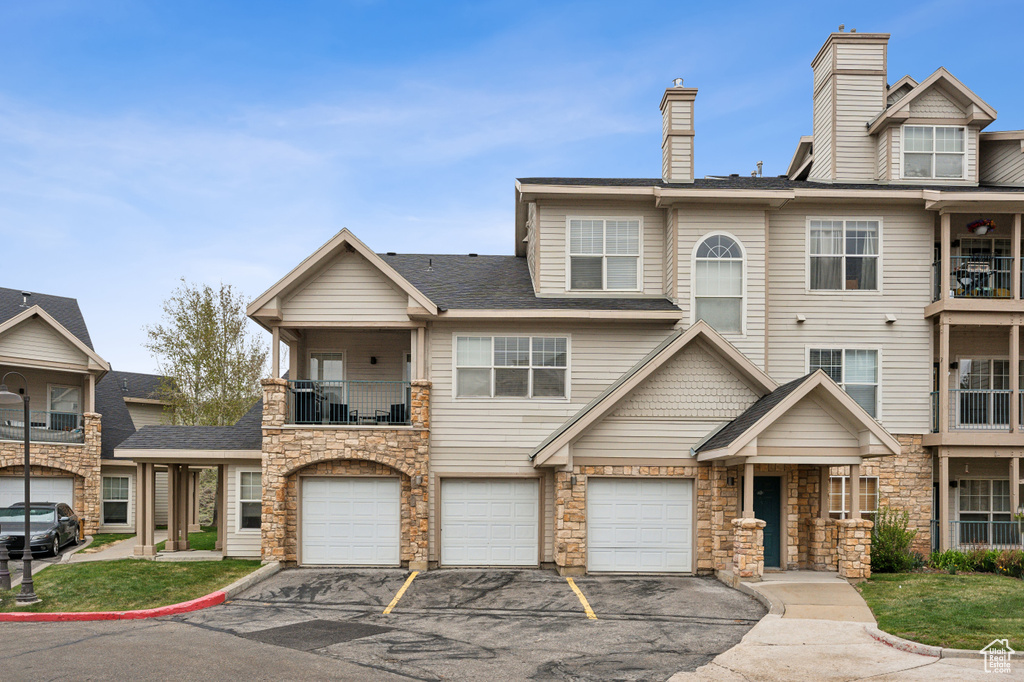 Multi unit property featuring a balcony, driveway, a garage, and stone siding