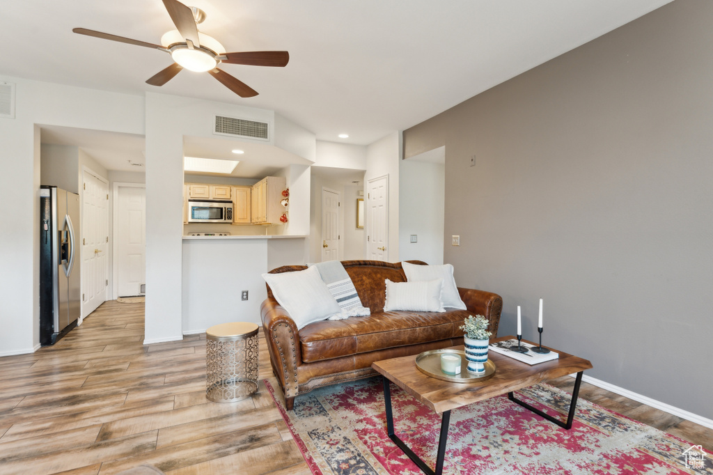 Living room with light wood-type flooring, baseboards, visible vents, and a ceiling fan