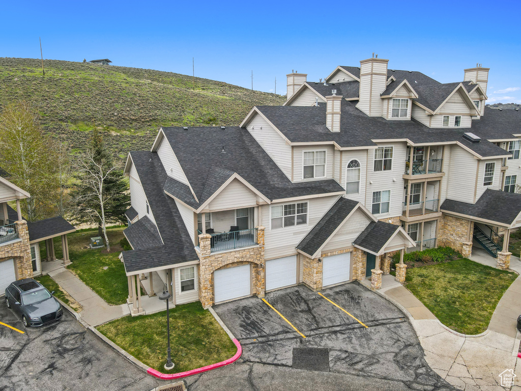 View of front of property with a balcony, driveway, a garage, stone siding, and roof with shingles
