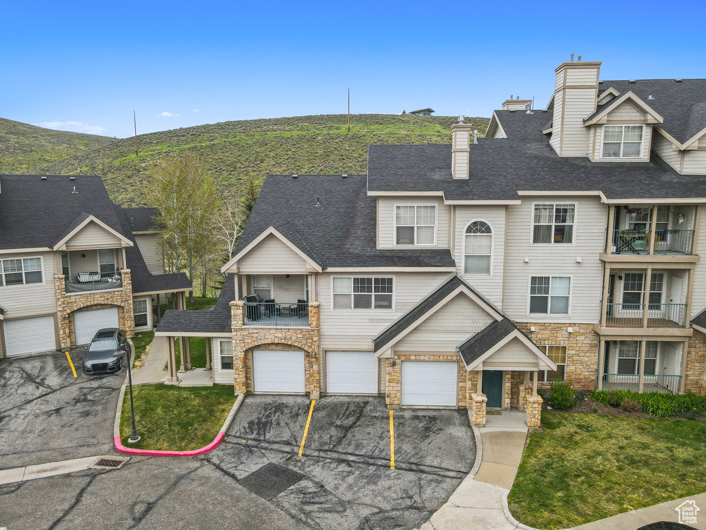 Townhome / multi-family property with stone siding, driveway, an attached garage, and a balcony