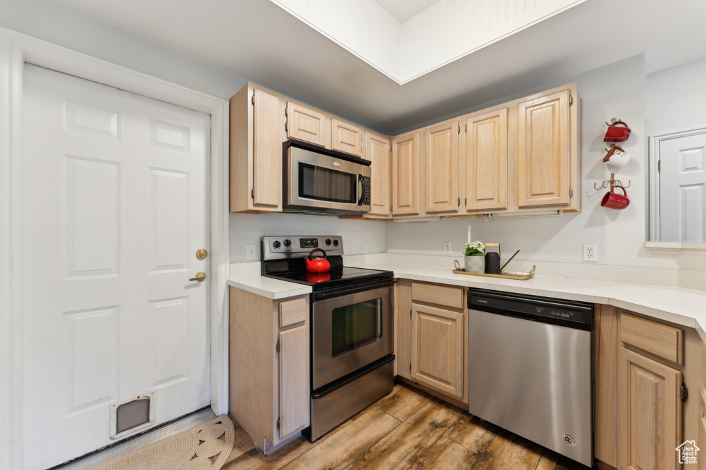Kitchen with light wood-type flooring, light countertops, light brown cabinetry, and appliances with stainless steel finishes