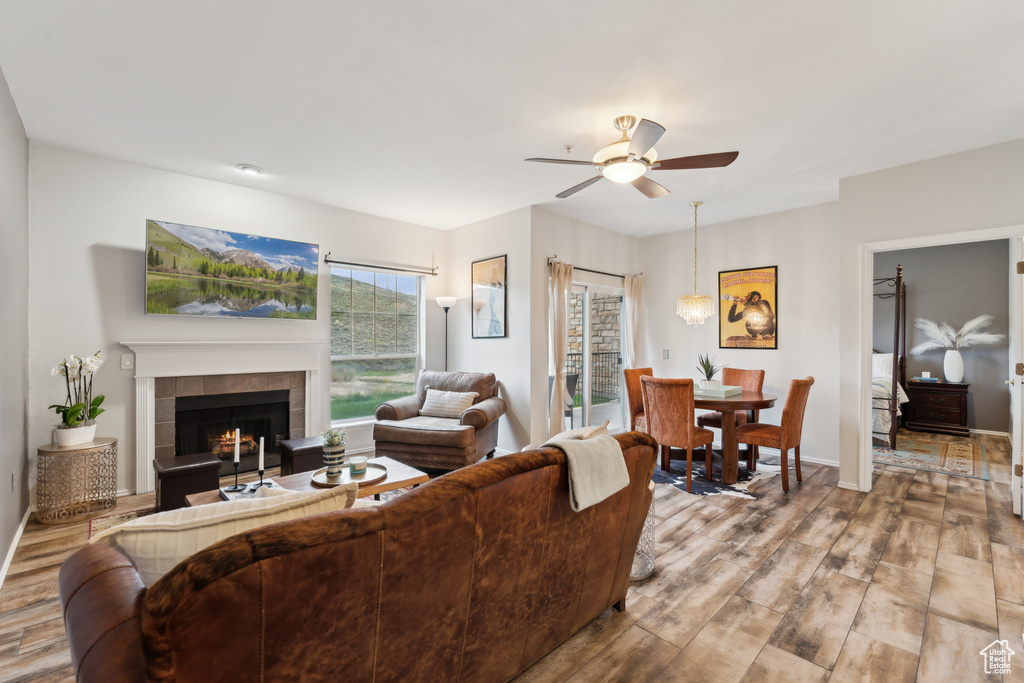Living room with ceiling fan, baseboards, a tiled fireplace, and wood finished floors