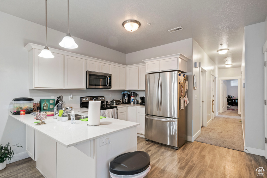 Kitchen with appliances with stainless steel finishes, a peninsula, white cabinets, light wood finished floors, and light countertops