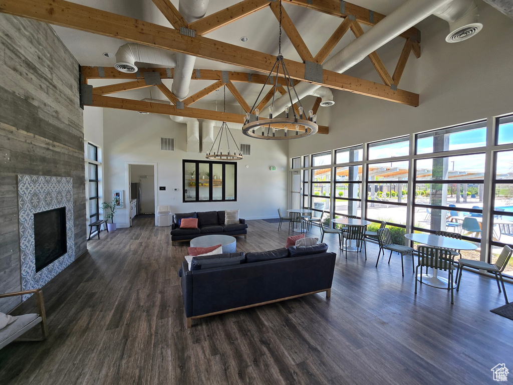 Living area with high vaulted ceiling, healthy amount of natural light, beam ceiling, a chandelier, and wood finished floors