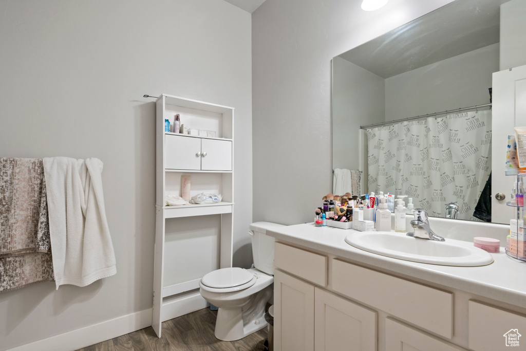 Bathroom with toilet, wood finished floors, vanity, a shower with curtain, and baseboards