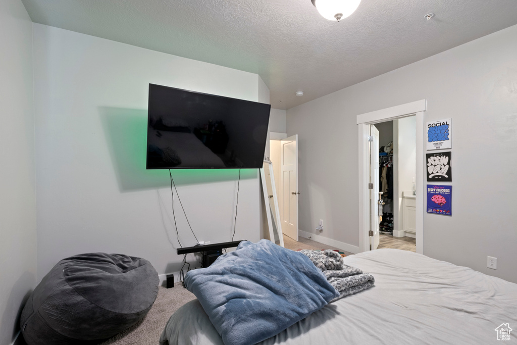 Bedroom featuring baseboards, light colored carpet, a spacious closet, a textured ceiling, and a closet