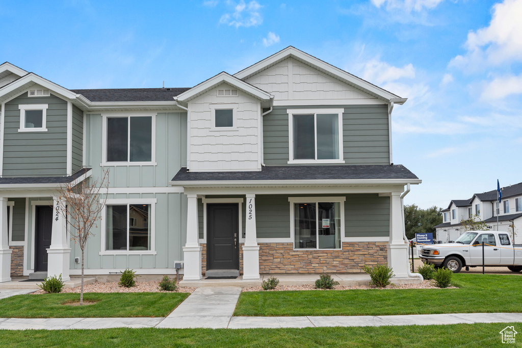 Craftsman-style home featuring stone siding, board and batten siding, a front yard, covered porch, and a shingled roof