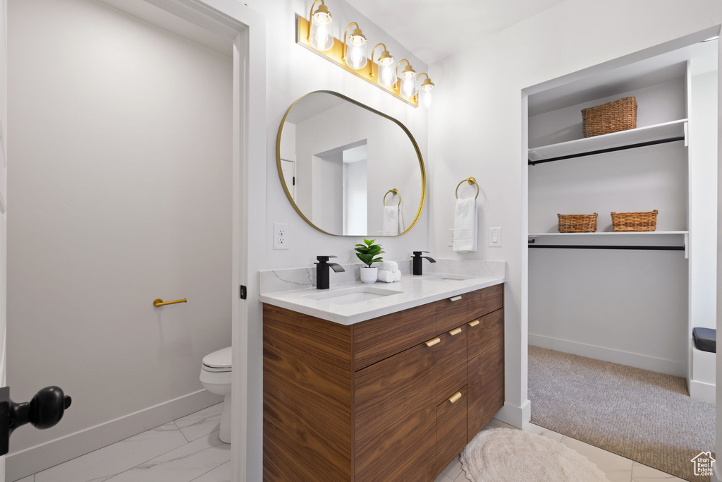 Bathroom with baseboards, toilet, double vanity, and marble look tile flooring