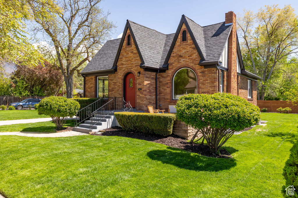 Tudor home featuring brick siding, a chimney, and roof with shingles