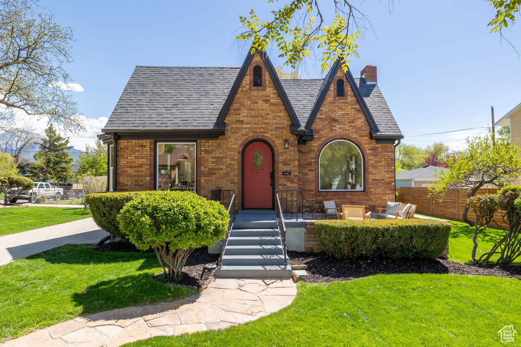 Tudor-style house with roof with shingles, brick siding, and a chimney