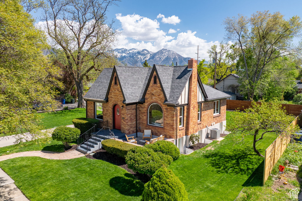 Tudor-style house with a chimney, brick siding, a mountain view, a shingled roof, and cooling unit