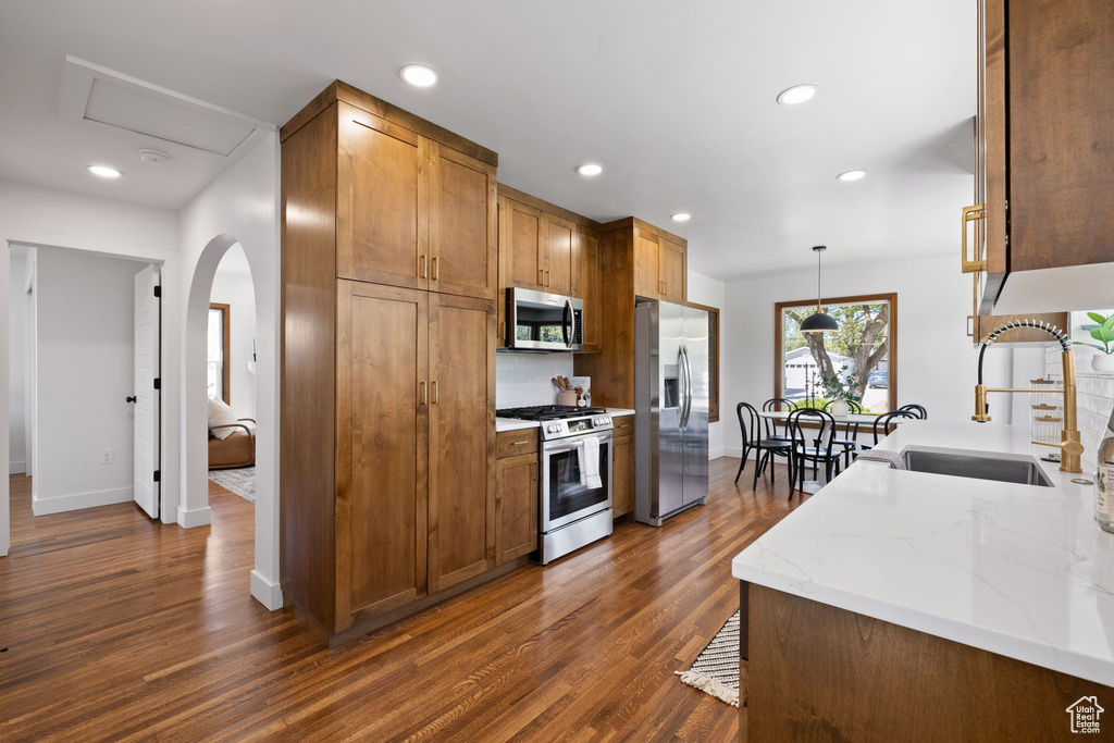 Kitchen with appliances with stainless steel finishes, a sink, baseboards, dark wood-type flooring, and brown cabinetry