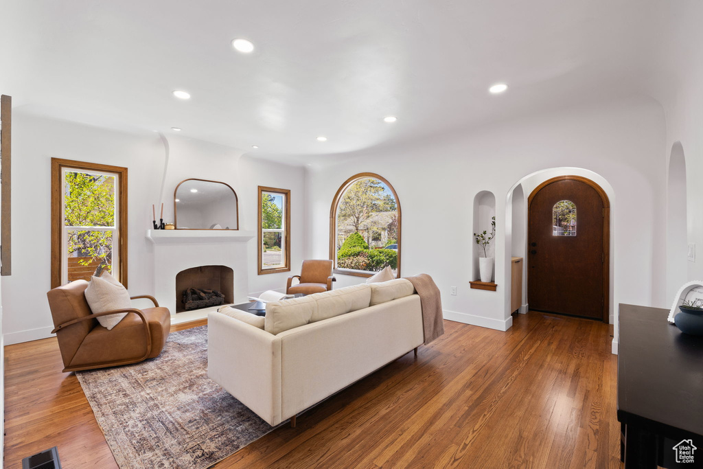 Living area featuring arched walkways, wood finished floors, recessed lighting, a fireplace with raised hearth, and baseboards