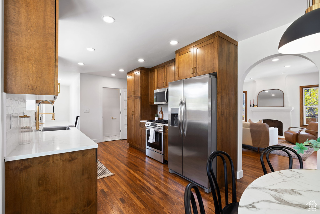 Kitchen featuring stainless steel appliances, a sink, dark wood-type flooring, arched walkways, and recessed lighting