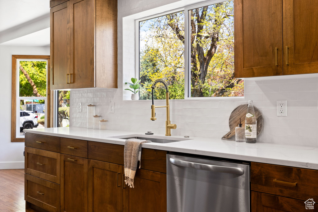 Kitchen with stainless steel dishwasher, tasteful backsplash, baseboards, a sink, and wood finished floors