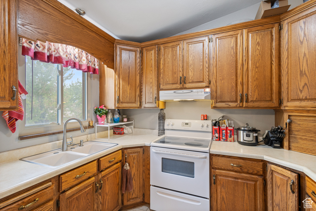 Kitchen with white electric stove, under cabinet range hood, a sink, brown cabinets, and lofted ceiling