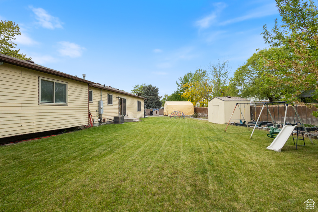View of yard with a storage unit, an outbuilding, a playground, and central air condition unit
