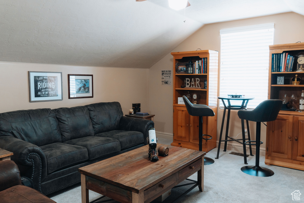 Living area featuring light carpet, vaulted ceiling, and a ceiling fan