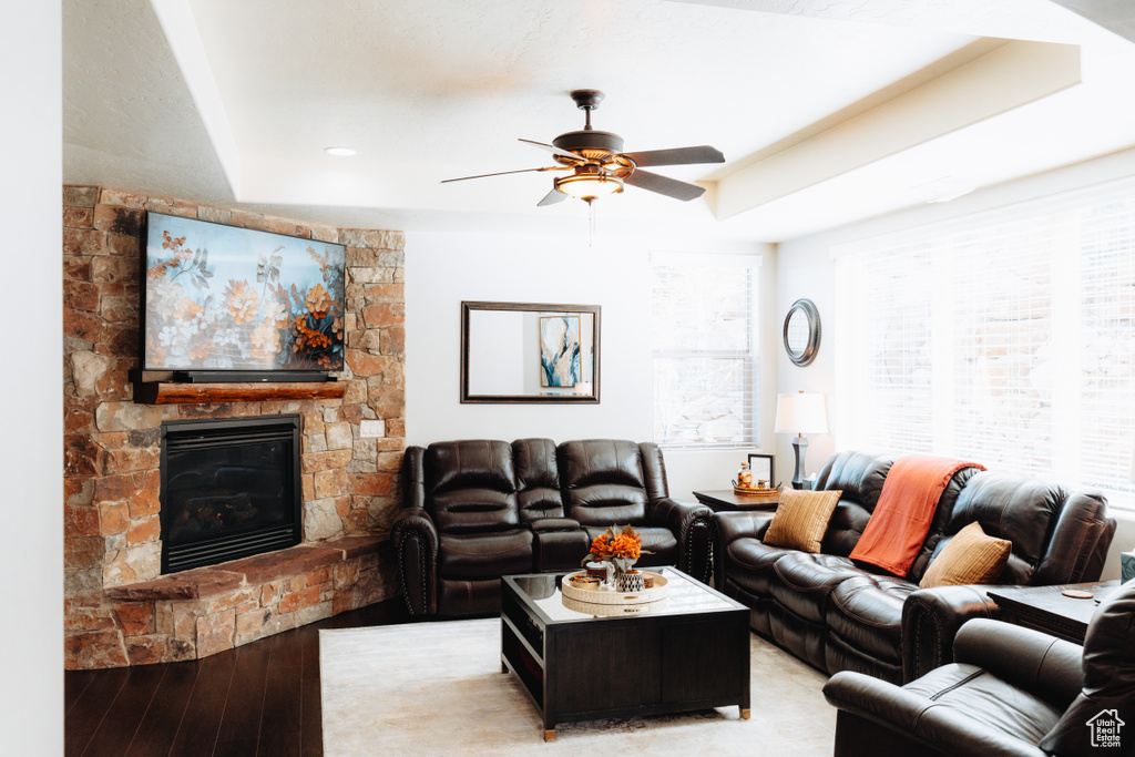 Living room featuring light wood-style floors, a stone fireplace, ceiling fan, and healthy amount of natural light