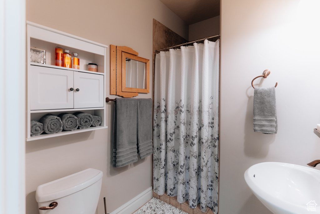 Bathroom with toilet, a shower with shower curtain, a sink, and baseboards